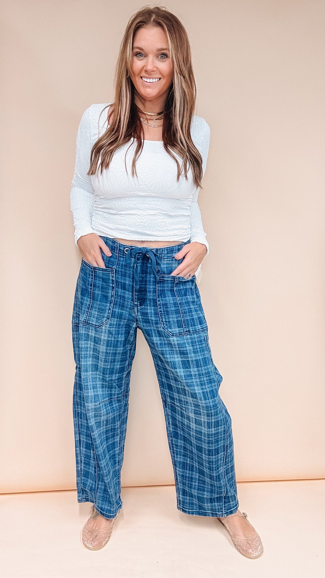 Woman wearing blue plaid pants and white long sleeve top on plain background