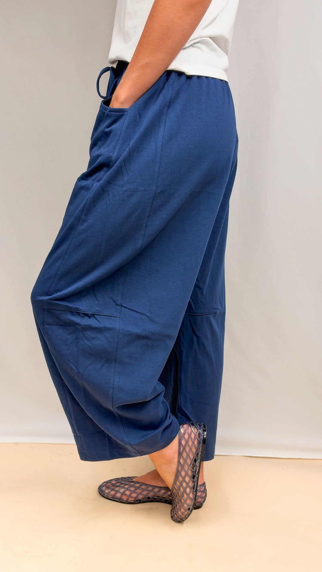 Woman wearing blue barrel sweatpants and white tee shown from side on plain background