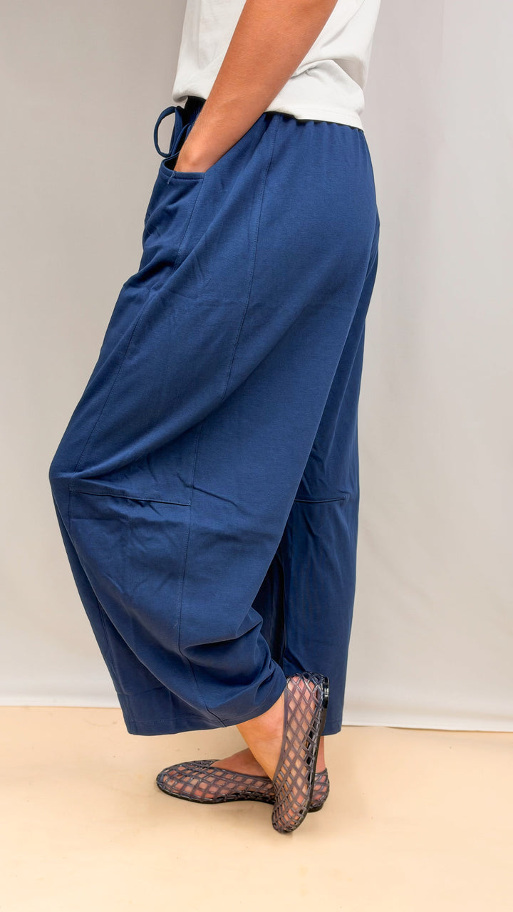 Woman wearing blue barrel sweatpants and white tee shown from side on plain background