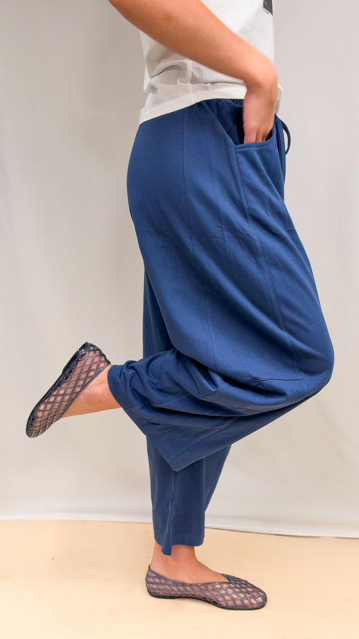 Woman shown from side view wearing blue barrel sweatpants and white tee on plain background