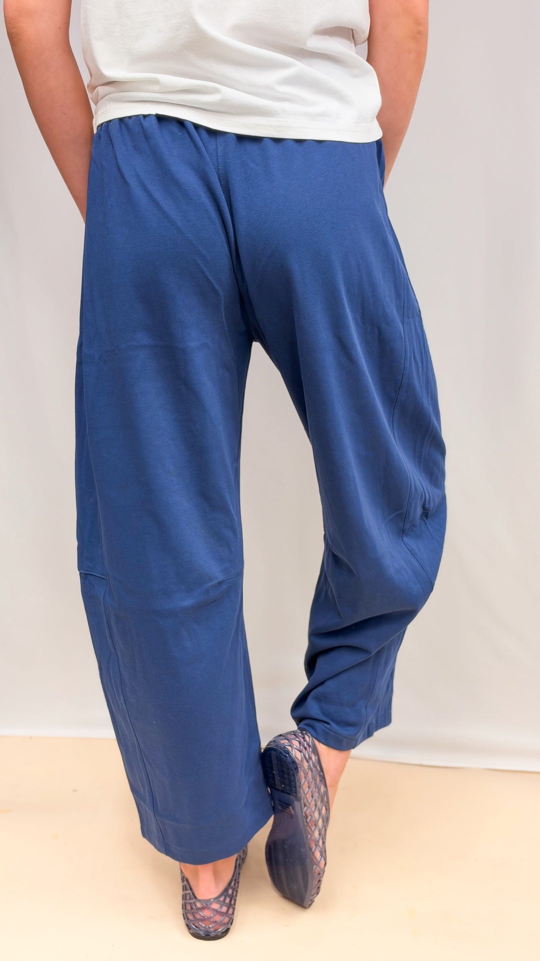 Woman shown from back view wearing blue barrel sweatpants and white tee on plain background