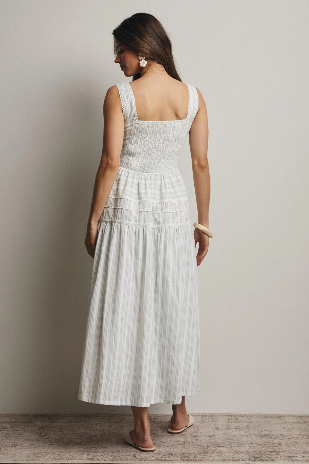 Woman wearing a white dress with thin straps against a plain background