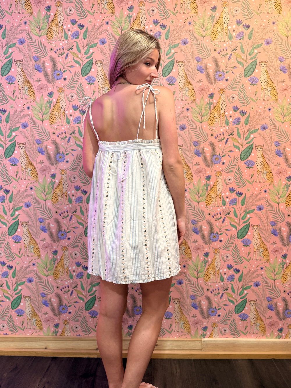 Woman in a white dress standing against a pink floral and animal patterned wall.