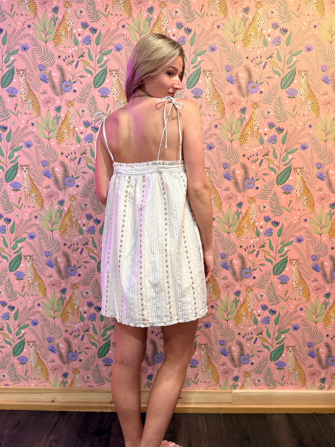 Woman in a white dress standing against a pink floral and animal patterned wall.