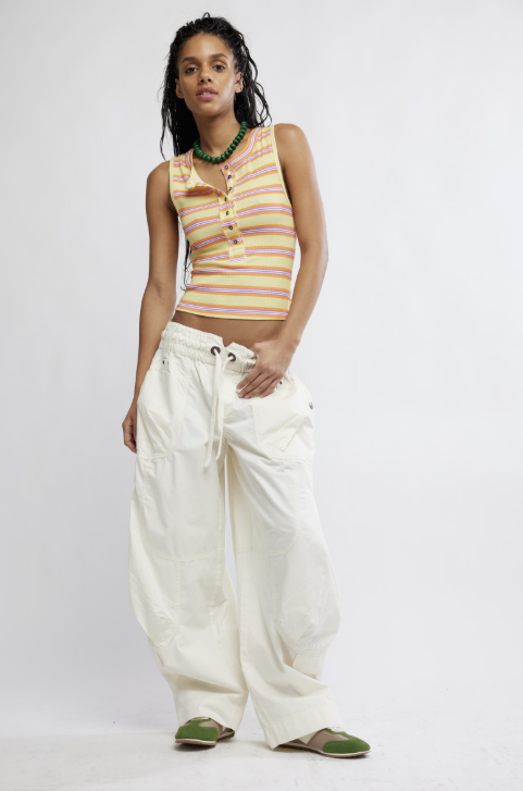 Woman wearing a striped sleeveless top and white pants on a plain background