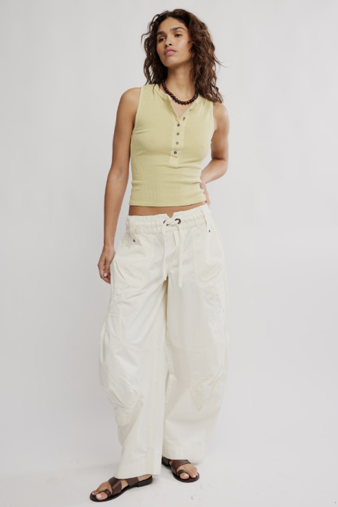 Woman wearing a light green sleeveless top and white pants on a plain background