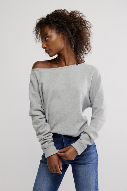 Woman wearing grey long sleeve top and jeans on white background