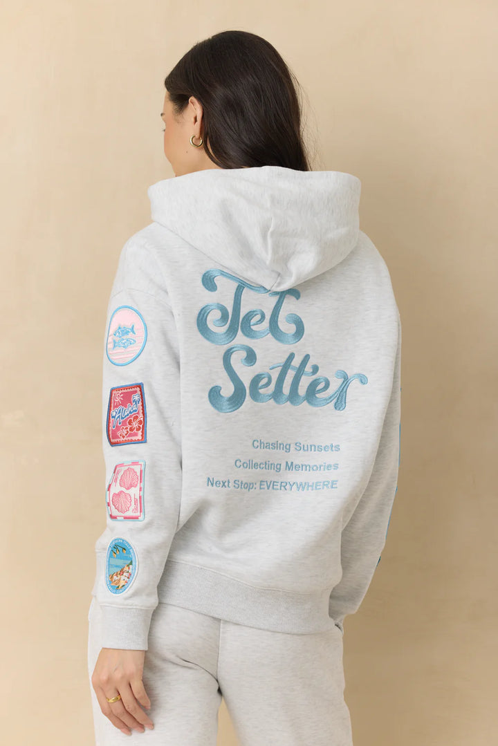 Woman wearing grey embroidered sweatshirt with patches on plain background