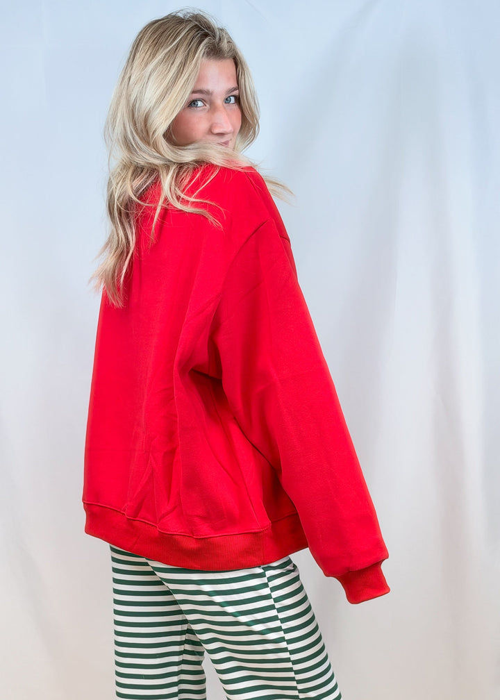 Woman shown from back view wearing red sweatshirt with green and white stripe pants on plain background