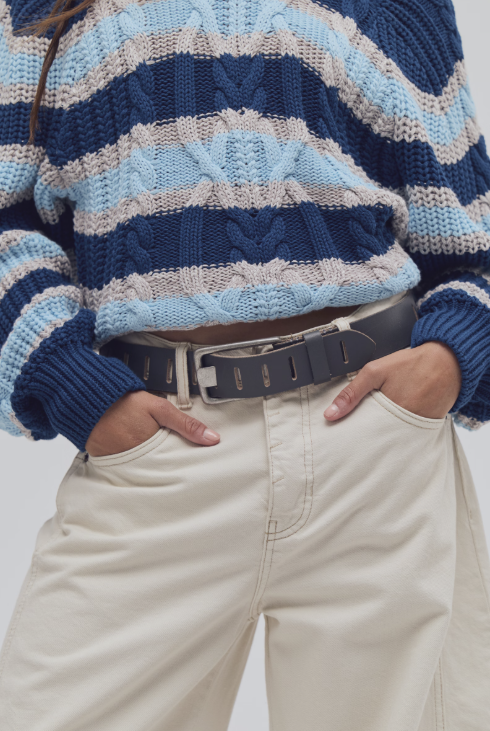 Woman wearing dark grey slotted belt with blue stripe sweater and beige pants