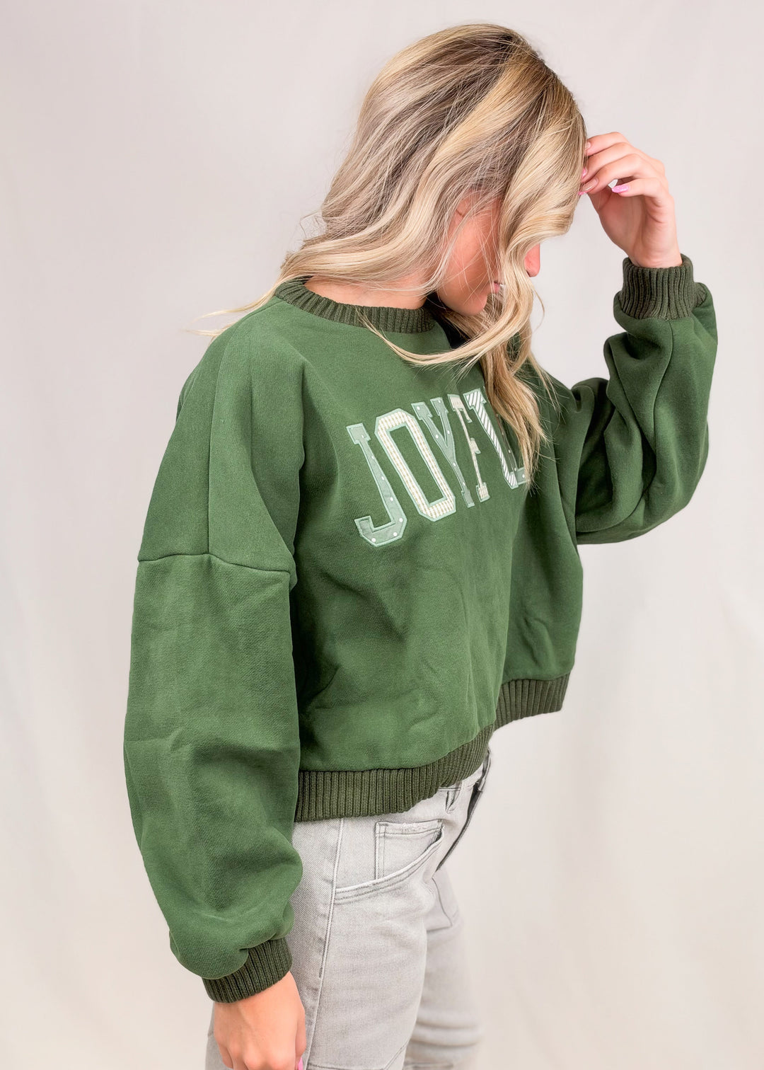 Woman wearing green mock neck sweatshirt and grey jeans on plain background