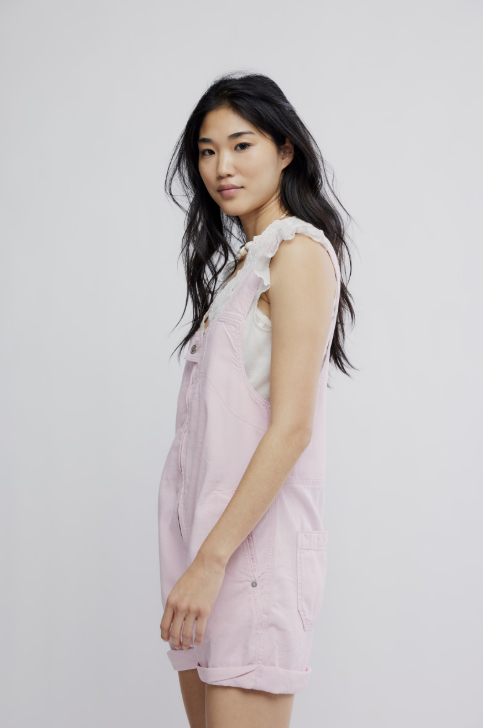 Woman wearing pink short overalls on plain background