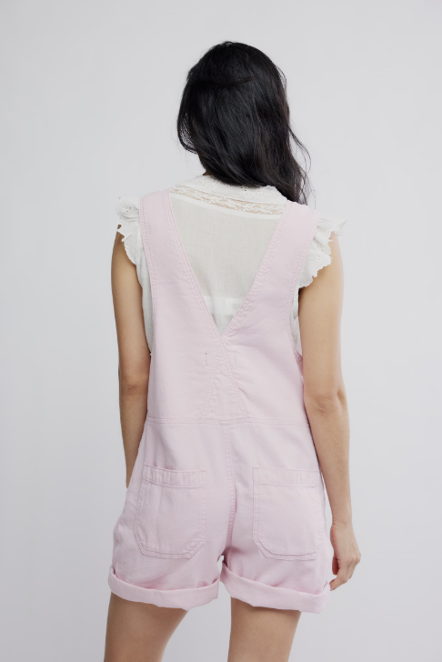 Person wearing a light pink denim romper with ruffled sleeves on a white background