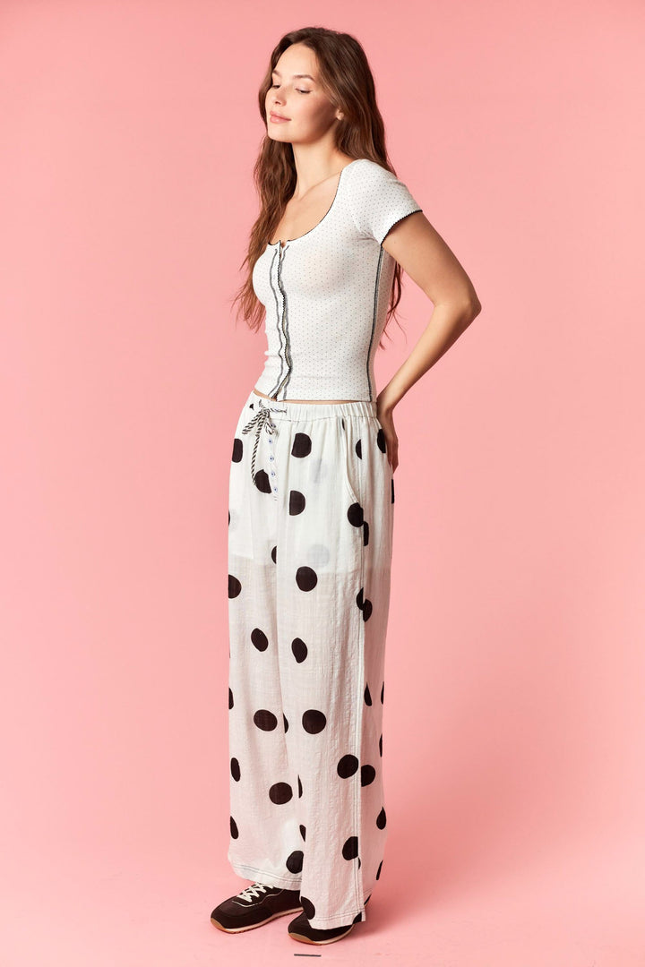 Woman wearing a white top and polka dot pants on a pink background