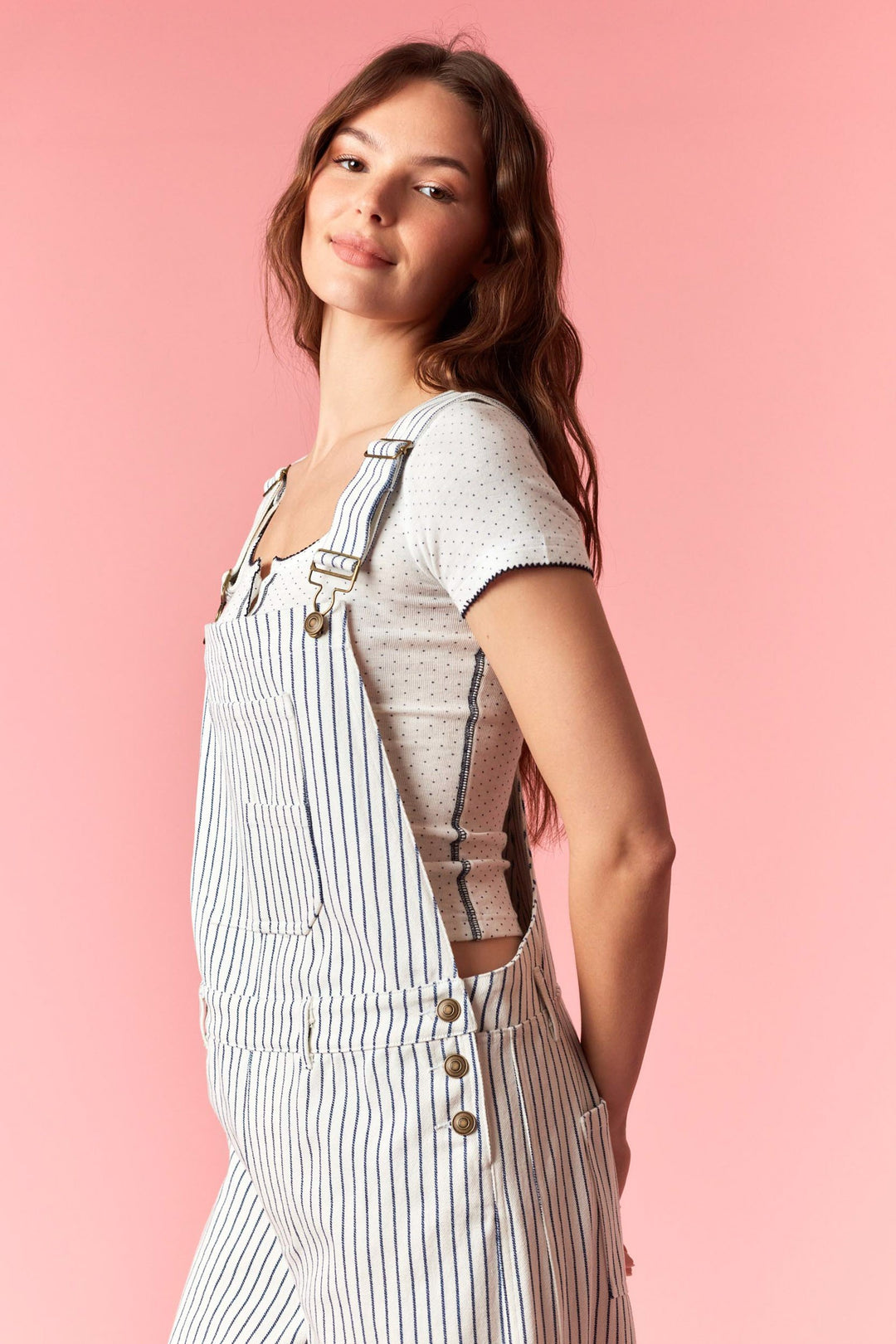 Woman wearing a striped overalls and t-shirt against a pink background