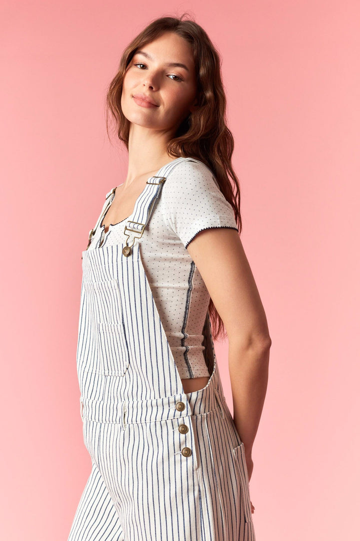 Woman wearing a striped overalls and t-shirt against a pink background