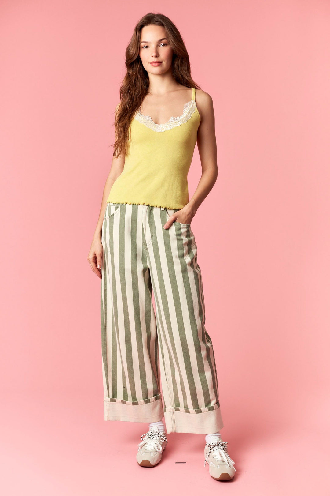 Woman wearing a yellow top and striped pants on a pink background
