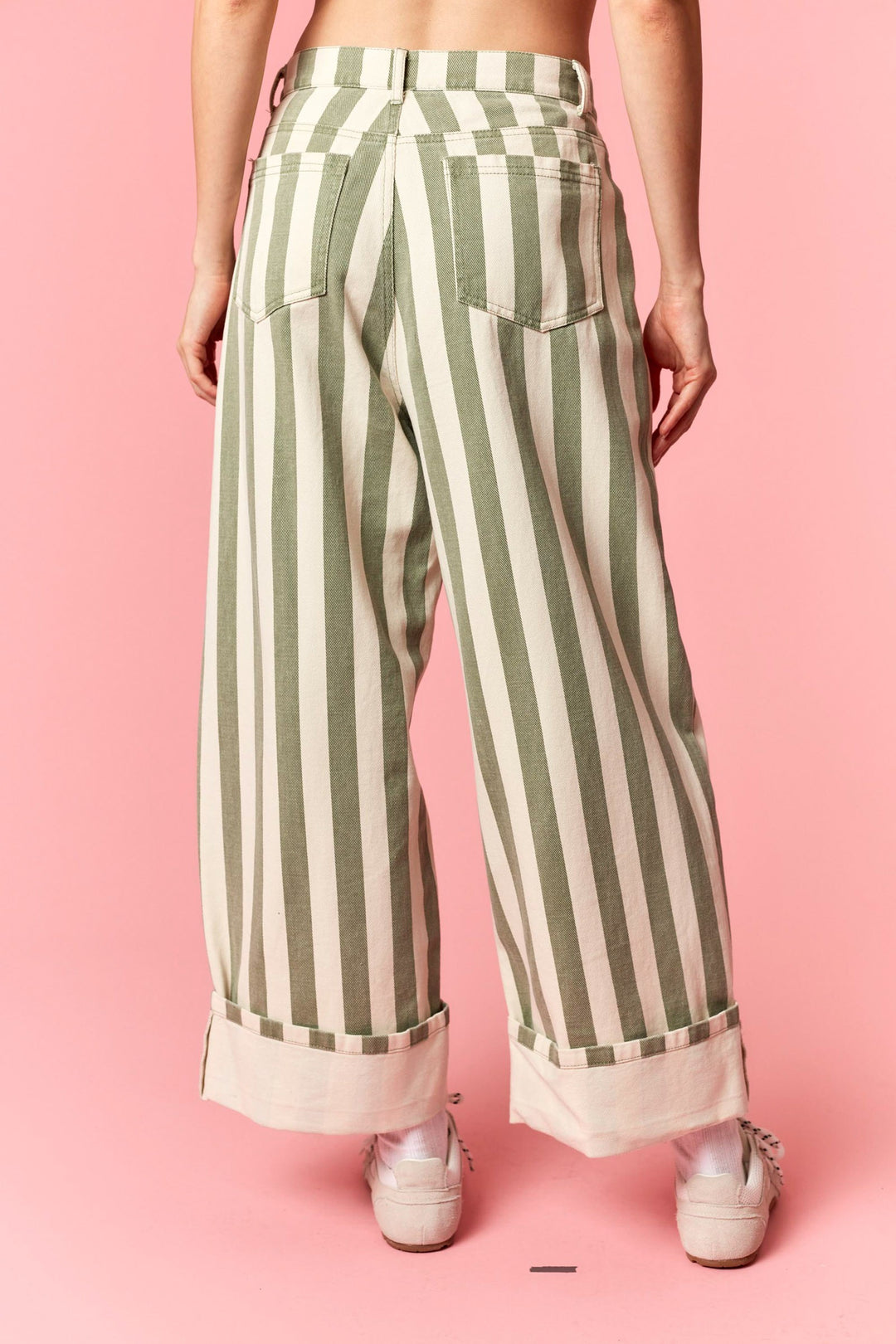 Green and white striped pants worn by a person on a pink background