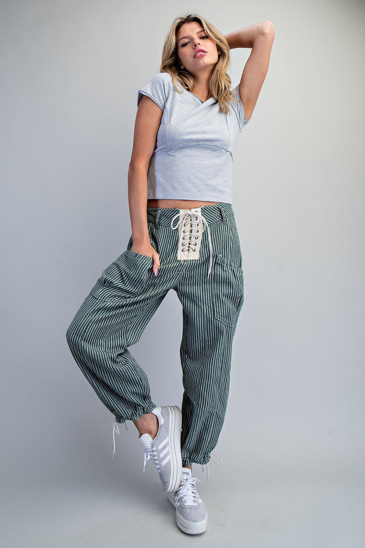 Woman wearing green stripe pants and grey top on plain background