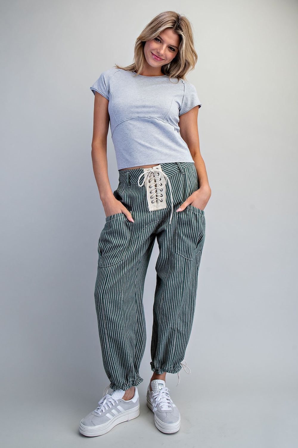 Woman wearing a light blue t-shirt and striped pants with white sneakers on a plain background