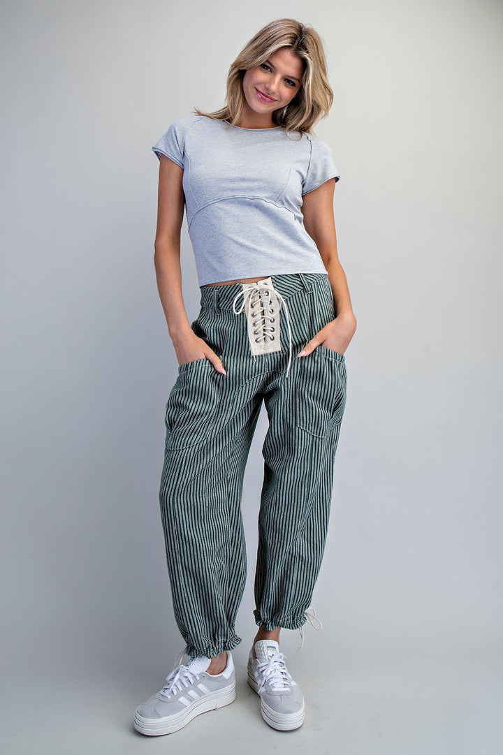 Woman wearing a light blue t-shirt and striped pants with white sneakers on a plain background