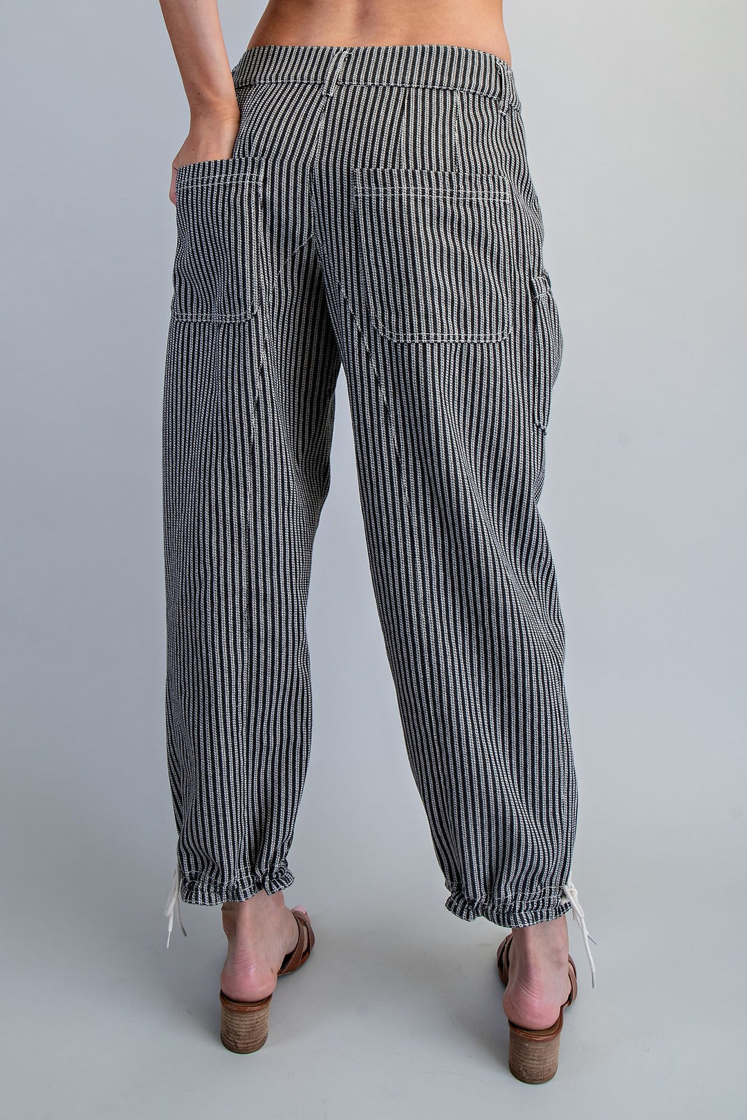 Woman wearing black and white pinstripe pants showing back pockets on plain grey background