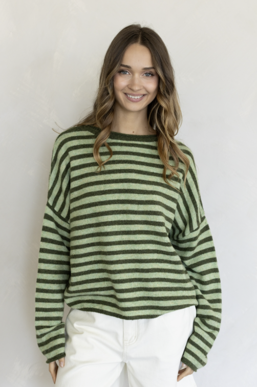 Woman wearing two tone green stripe sweater and white pants on plain background