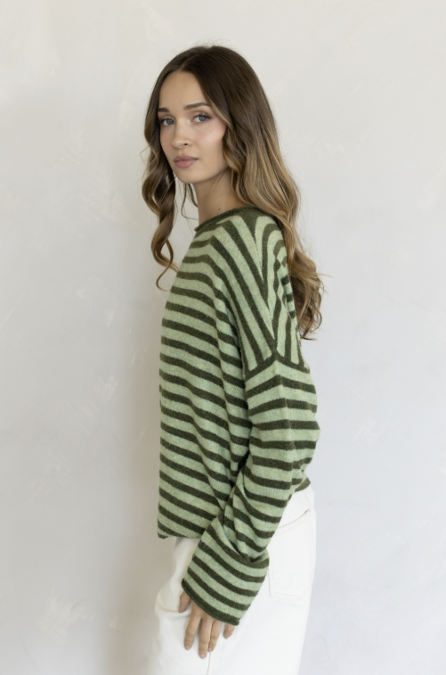 Woman wearing two tone green stripe sweater and white pants on plain background