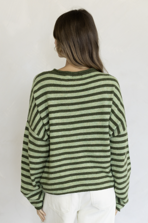 Woman shown from behind wearing two tone green stripe sweater and white pants on plain background