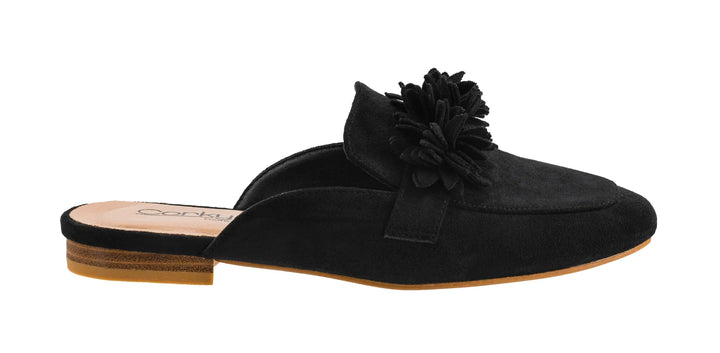 A black suede mule loafer with a large fabric flower embellishment on the vamp, shown in profile against a white background.