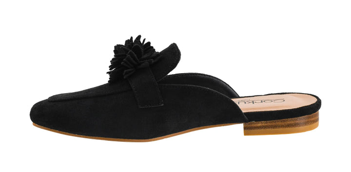 A black suede mule slipper with a large fabric flower embellishment on the strap, shown in profile against a white background.