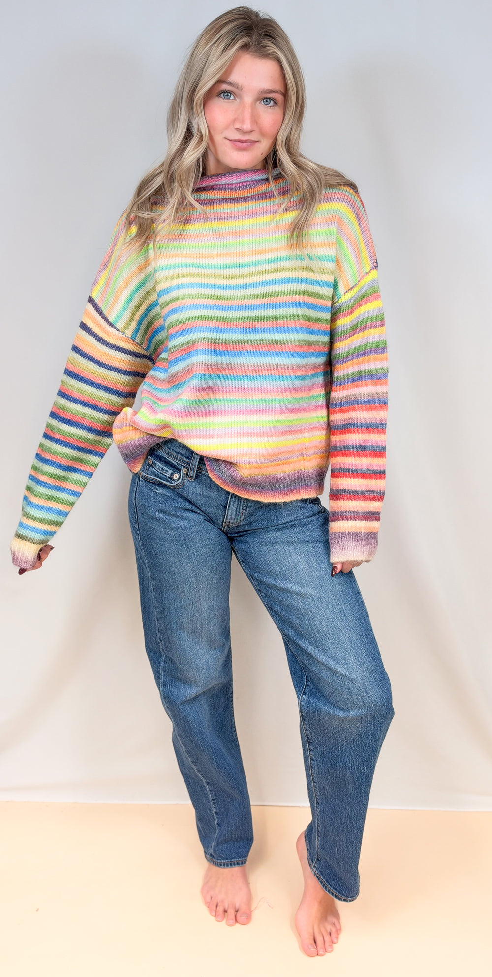 Woman wearing colorful stripe mock neck sweater with jeans on plain background