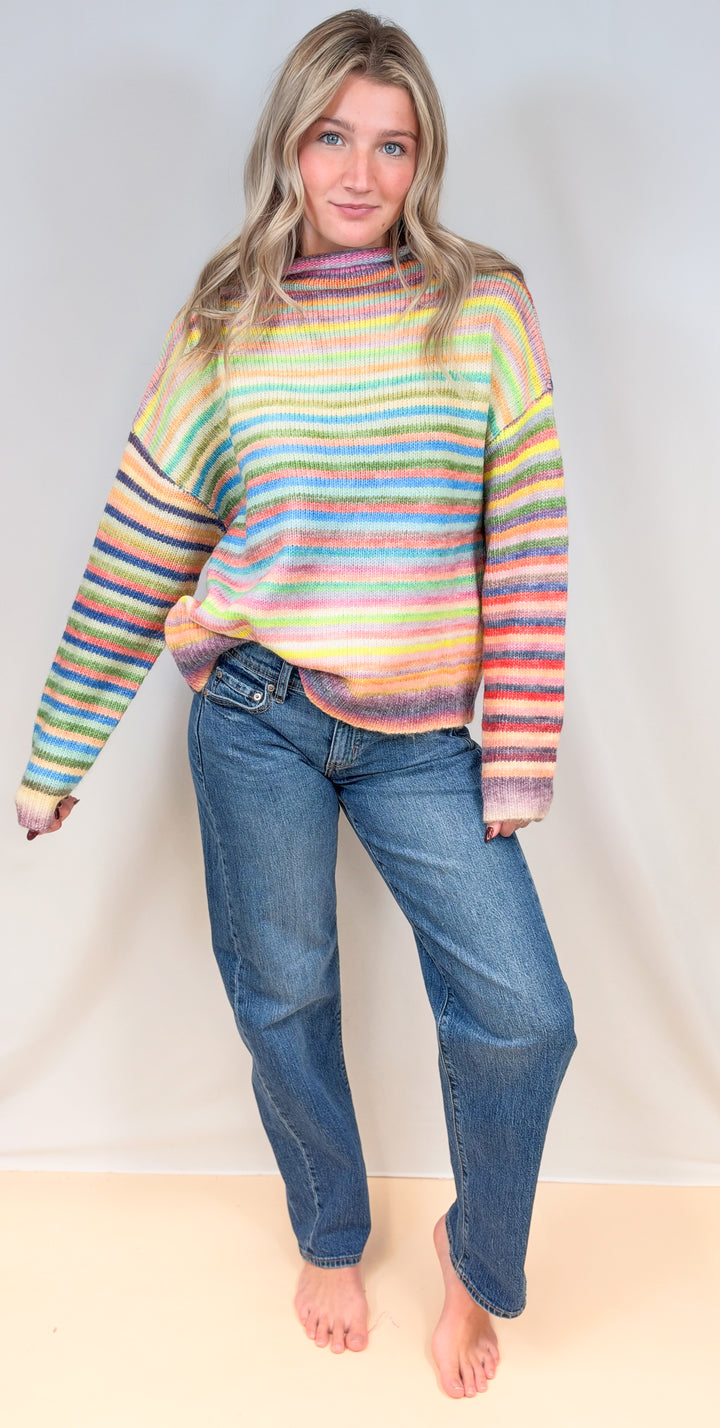 Woman wearing colorful stripe mock neck sweater with jeans on plain background