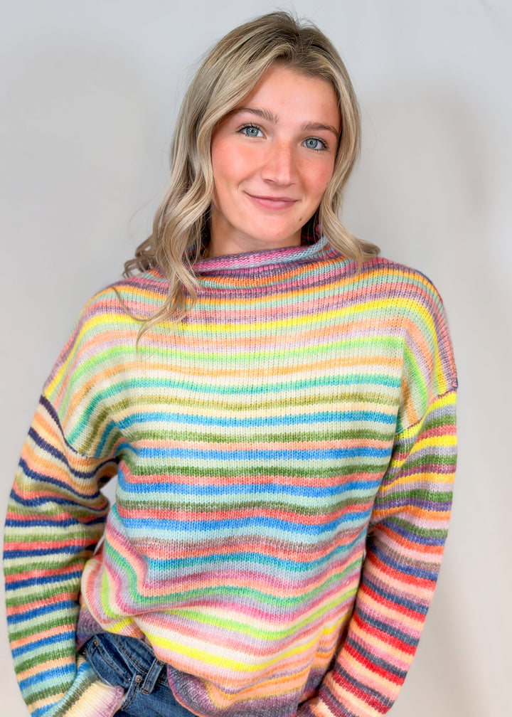 Woman wearing colorful stripe mock neck sweater on plain background