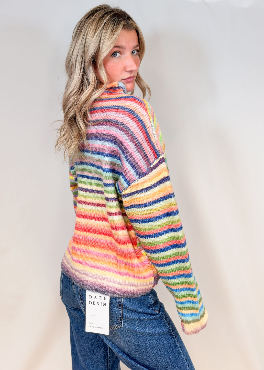 Woman wearing colorful stripe mock neck sweater with jeans on plain background