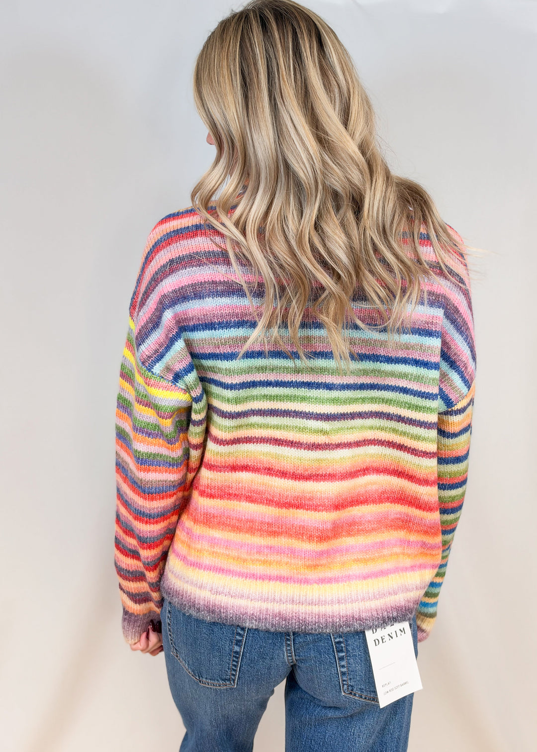 Woman wearing colorful stripe sweater with jeans on plain background