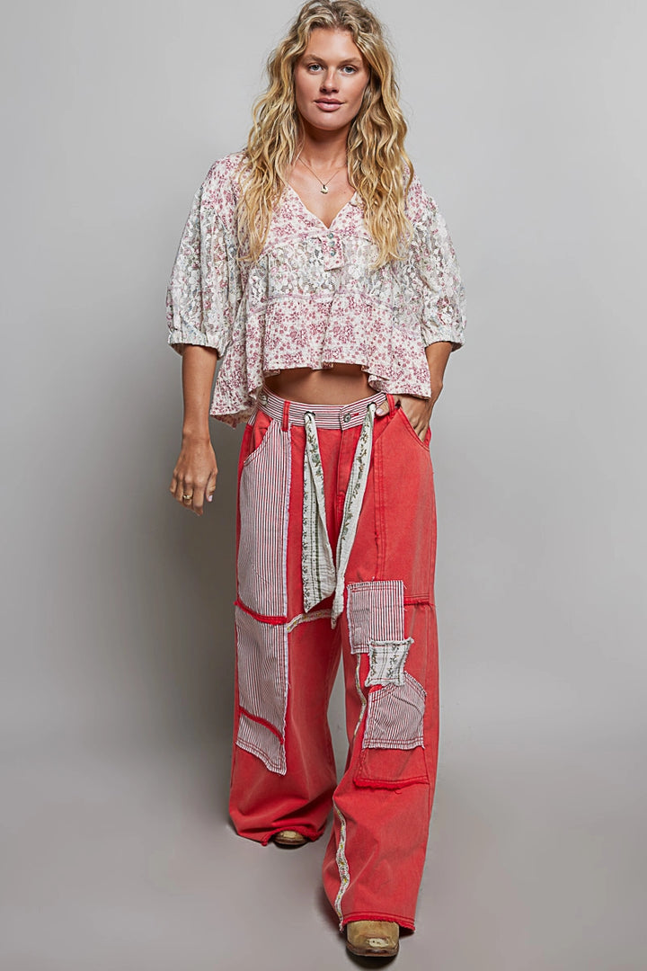 Woman wearing a floral top and red pants against a gray background