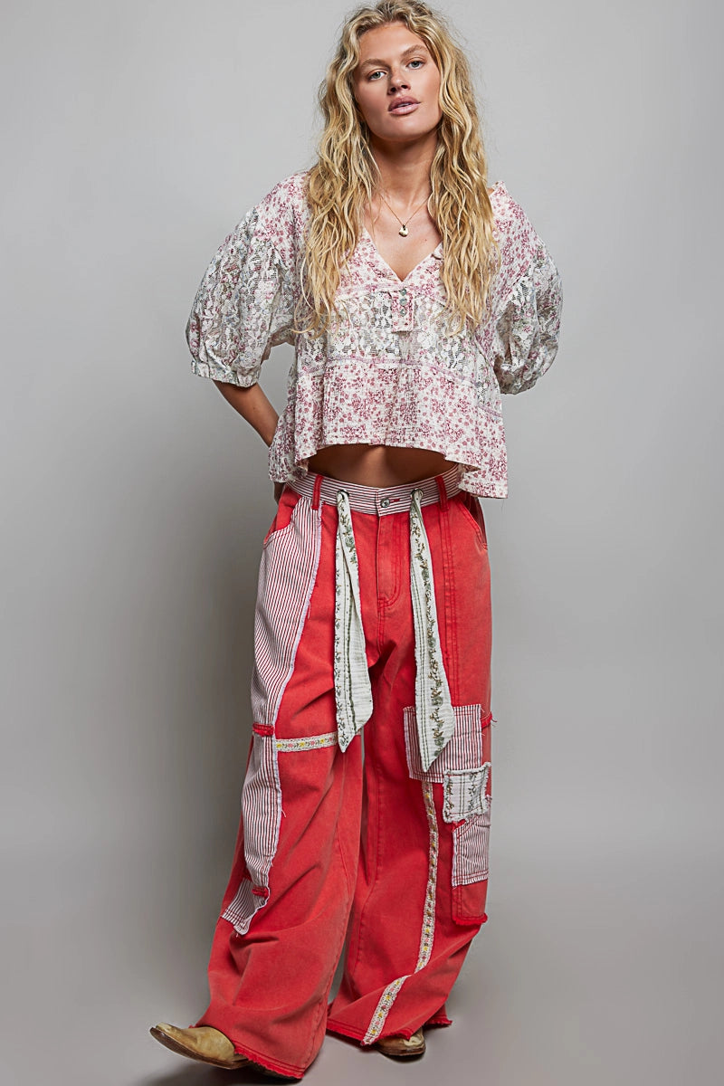 Woman wearing a patterned top and red pants against a gray background