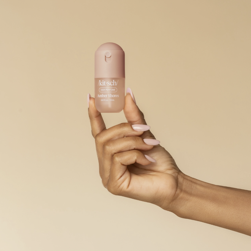Hand holding kitsch amber shores hair perfume on plain background