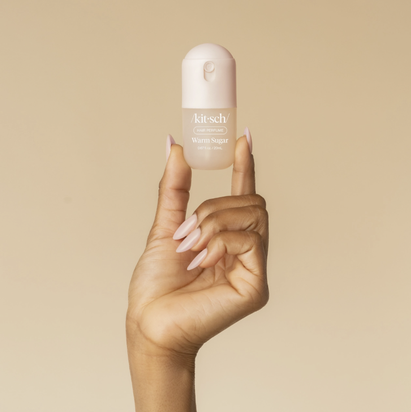 Hand holding mini kitsch hair perfume on plain background