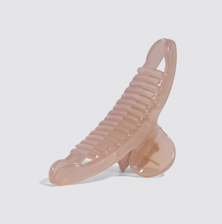 A translucent blush pink hair claw clip with a ribbed combing surface, shown on a clean light gray background.