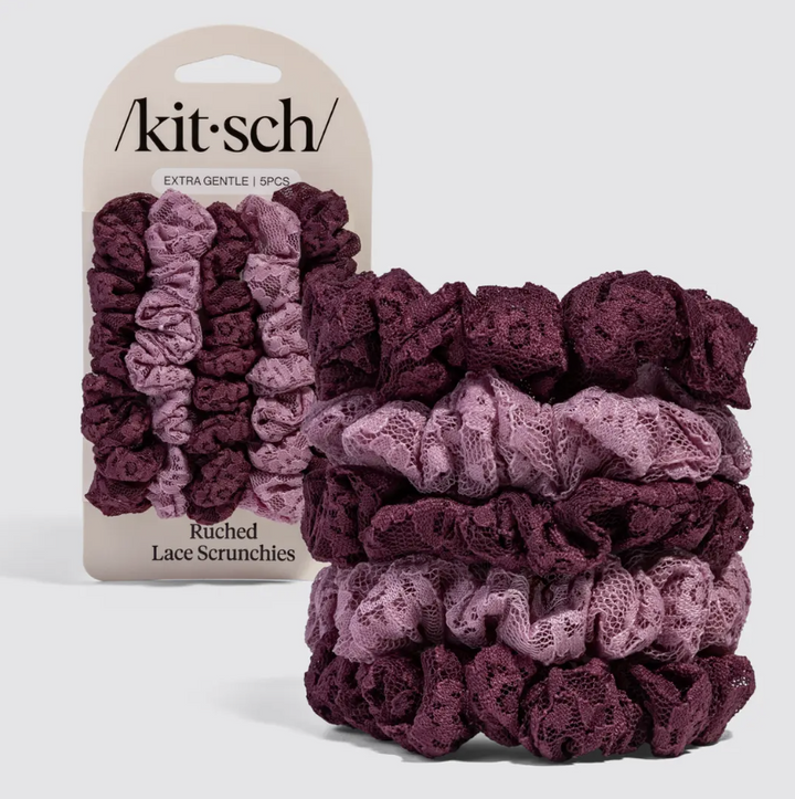 A set of six Kitsch lace scrunchies in shades of plum and mauve, shown with their original cardboard packaging on a light gray background.
