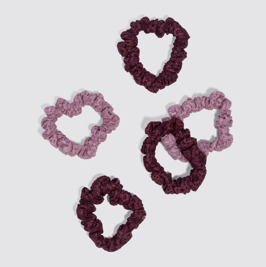 Five fabric scrunchies in two shades of purple (a dusty mauve-pink and a deep plum-burgundy) arranged on a light gray background.