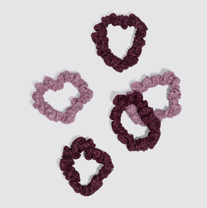 Five fabric scrunchies in two shades of purple (a dusty mauve-pink and a deep plum-burgundy) arranged on a light gray background.
