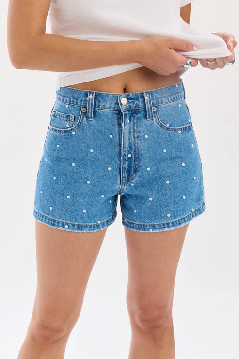 Woman wearing denim shorts with polka dots and white tee on white background