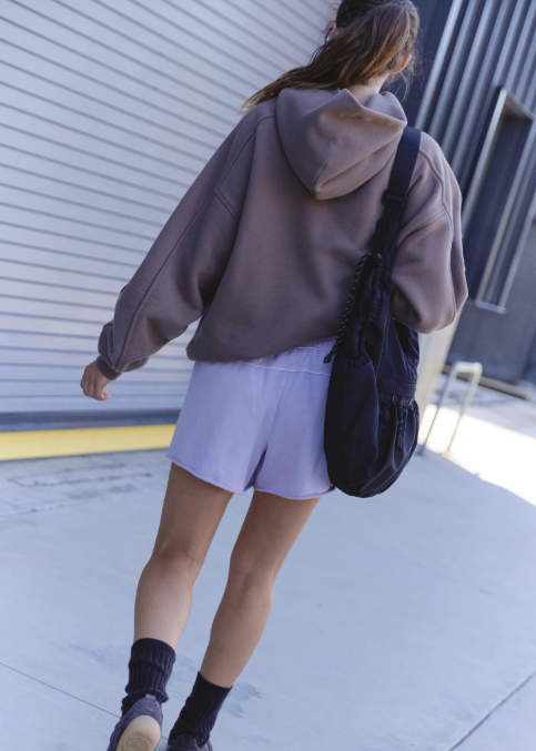 Woman shown from back wearing purple sweat shorts and brown sweatshirt walking outdoors