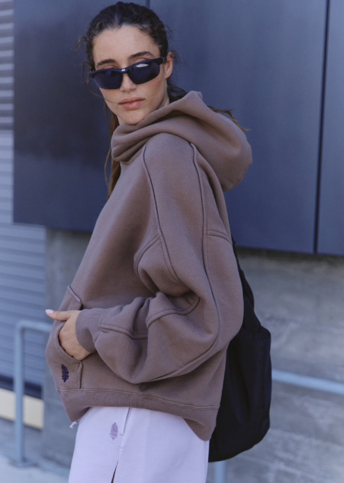 Woman wearing light purple sweat shorts and brown sweatshirt standing outdoors