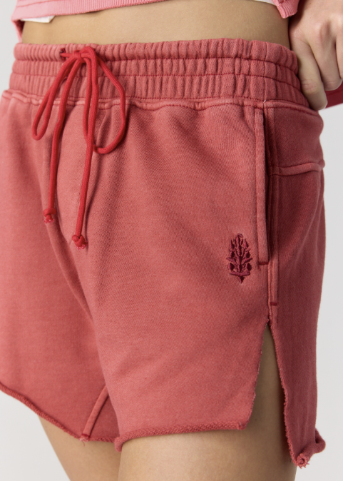 Close up of woman wearing pink sweatshirt and red sweat shorts on plain background