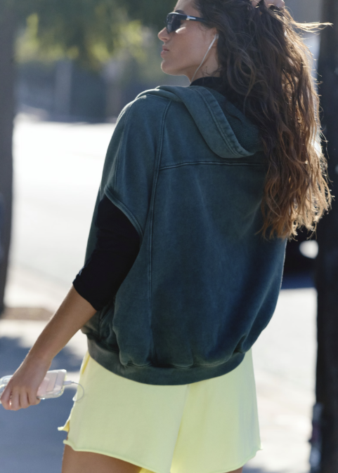 Woman shown from back walking outdoors wearing lime green shorts with hunter green vest 