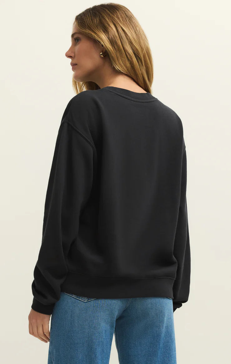 Person wearing a black sweatshirt and blue jeans on a beige background